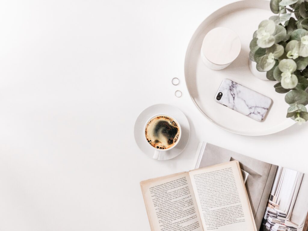 A cup of coffee near books and magazines on a white background