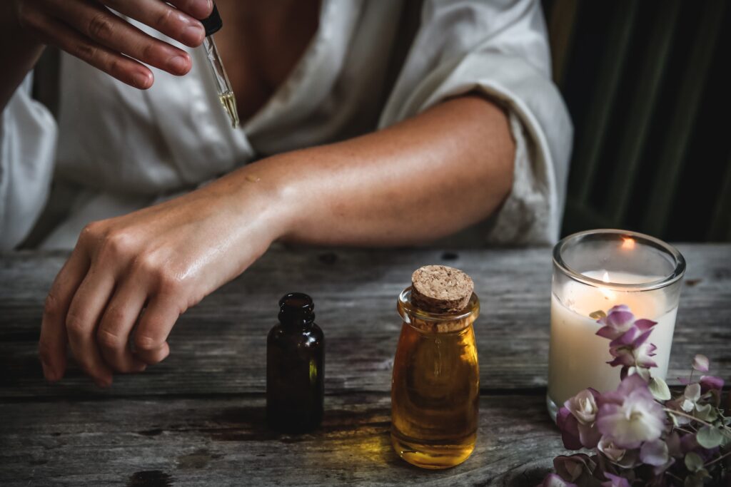 Woman adds a tincture to her arm in front of a candle and flowers