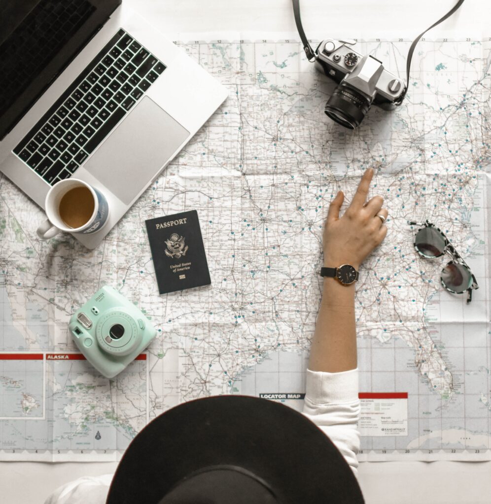 Woman with a large hat pointing to a location on a map with her laptop beside her. 