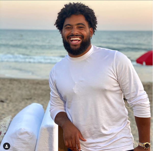 male cbd business owner, nico marley, stood in a white shirt on a beach