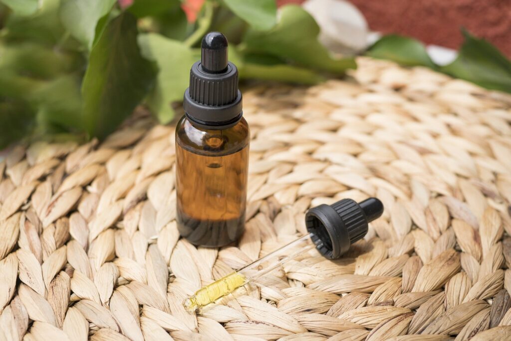 A brown bottle of tincture on a wicker mat with the dropper lying beside it. The dropper contains a small dose of yellow CBD oil.