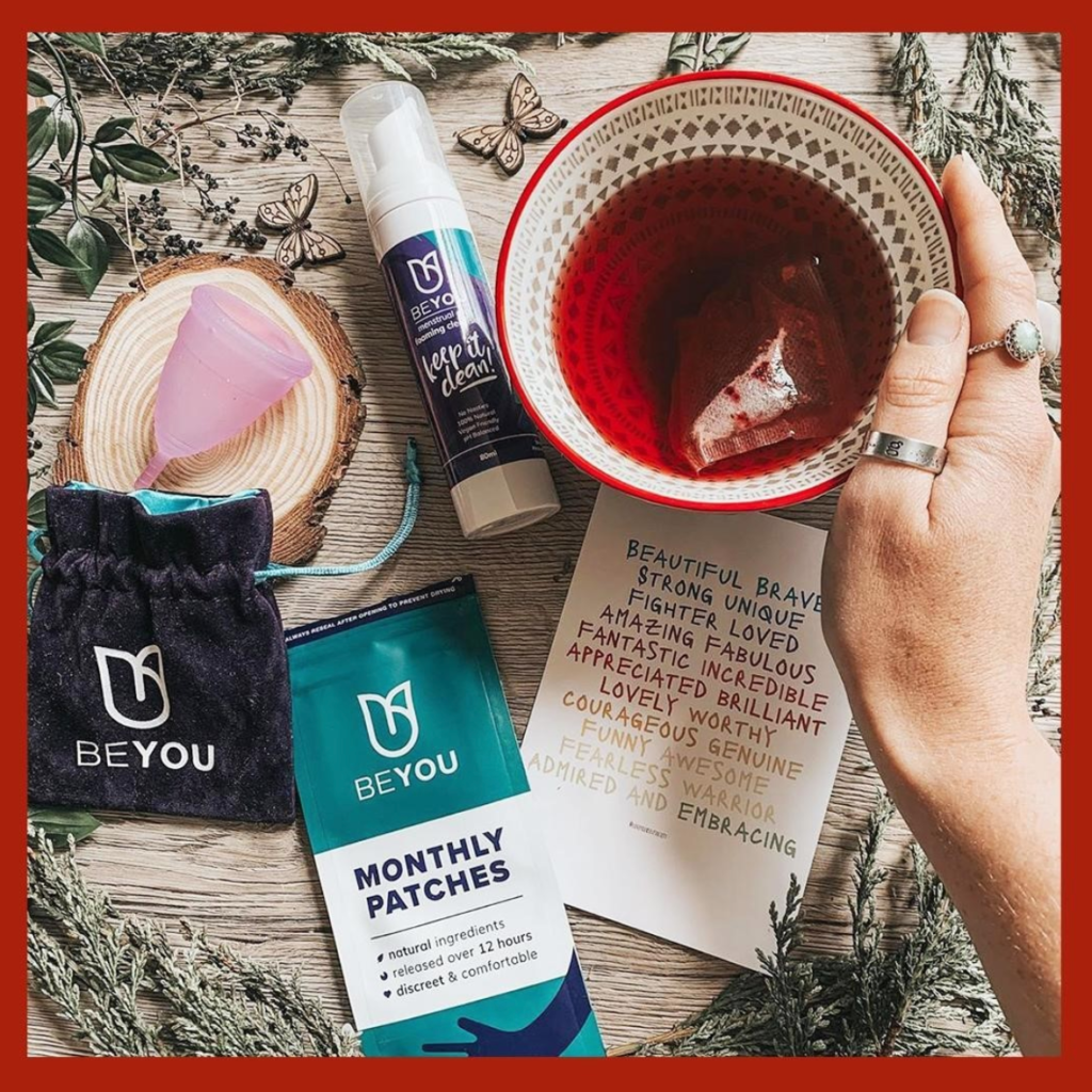 Be you period patches, a period cup and pain relief near a cup of herbal tea with a christmas theme.