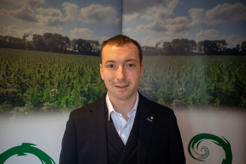 A man wearing a black suit is pictured in front of a green field. 