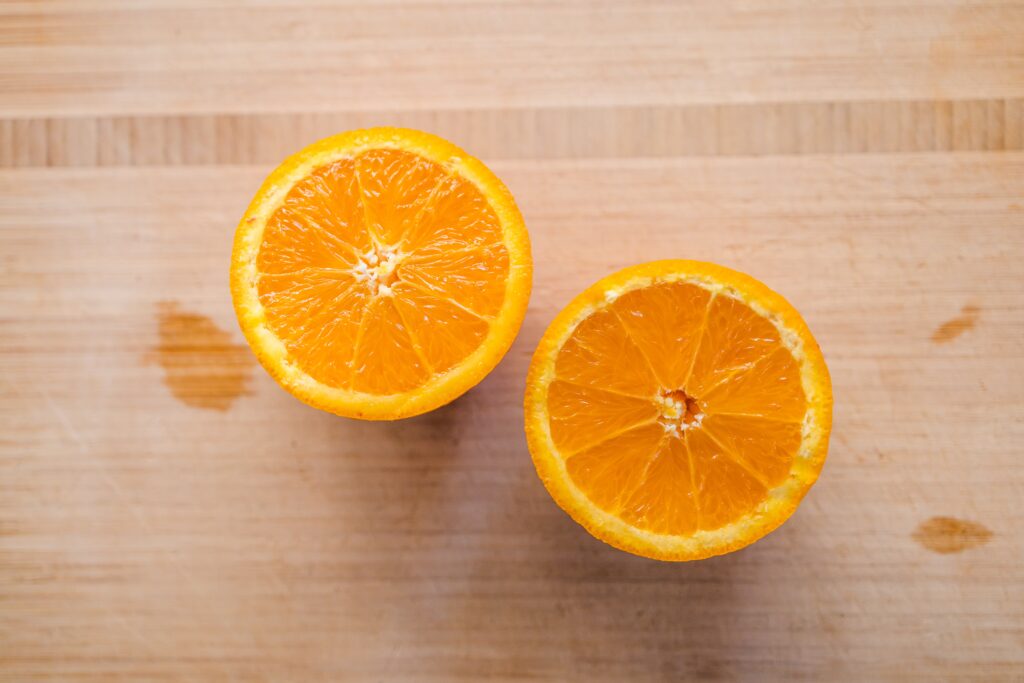 An orange cut in half on a wooden chopping board