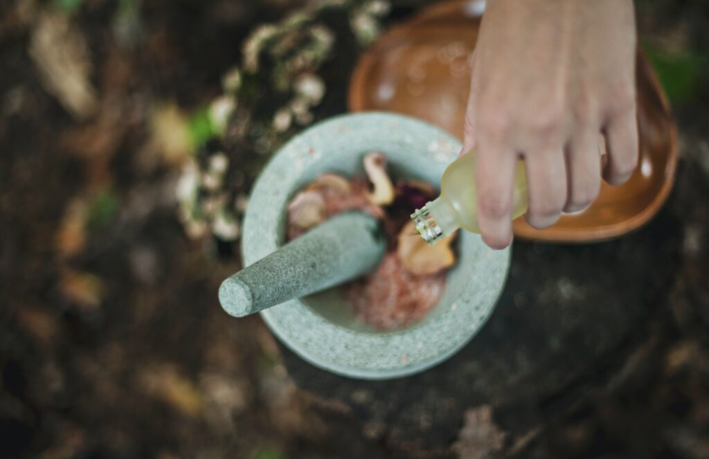 A hand pours a bottle of oil into a bowl of petals