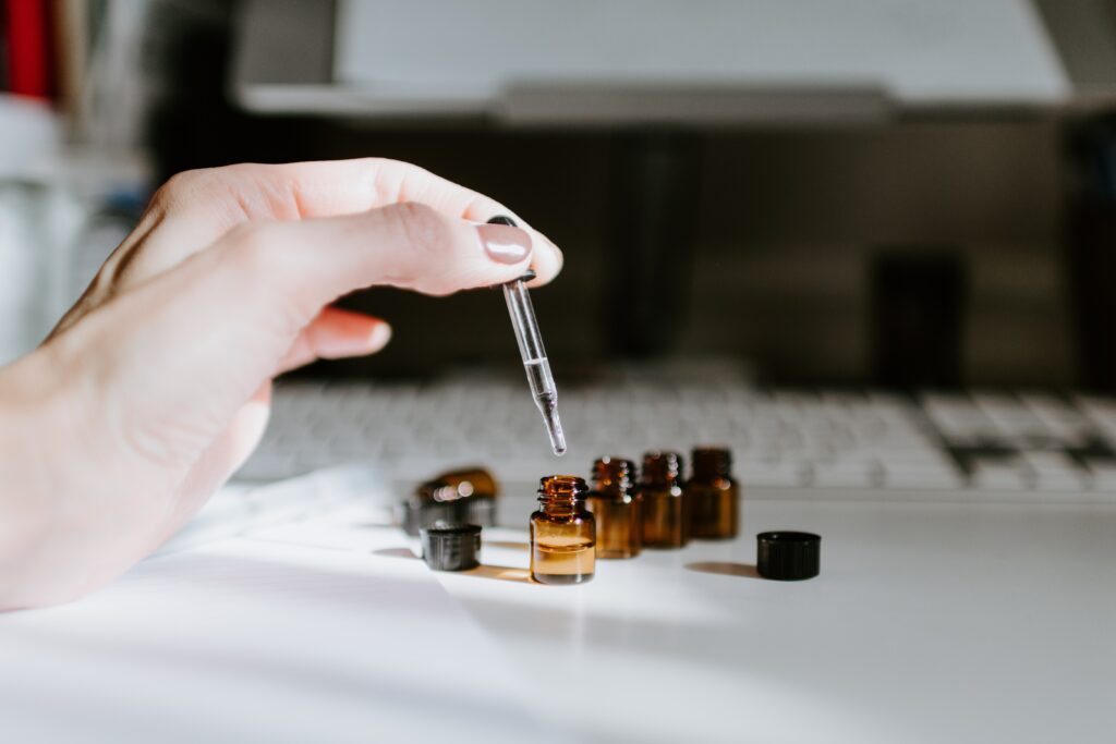 A white hand extended across the left of the photo holding a dropper while a line of miniature brown bottles of oil are in the background.