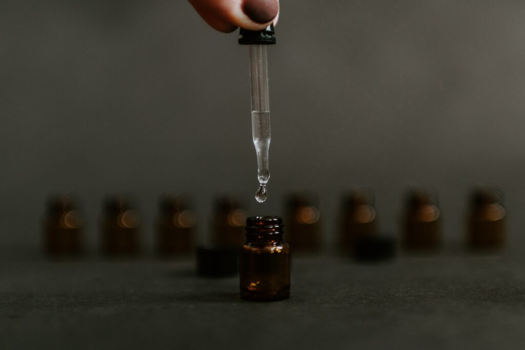 A row of brown oil bottles in the background while a hand holds a dropper above a bottle in the front 