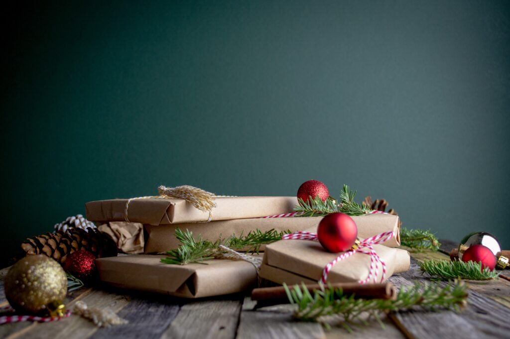 A pile of brown paper wrapped presents on the floor with baubles against a dark wooden background.