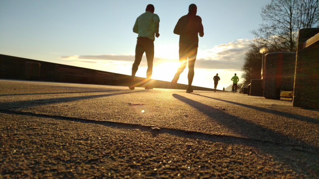 A series of runners against a bright sun on a pavement. 