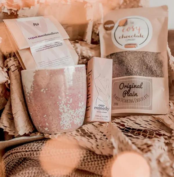 A pink and brown mug, oil and bag of hot chocolate sits on top of brown packaging. 