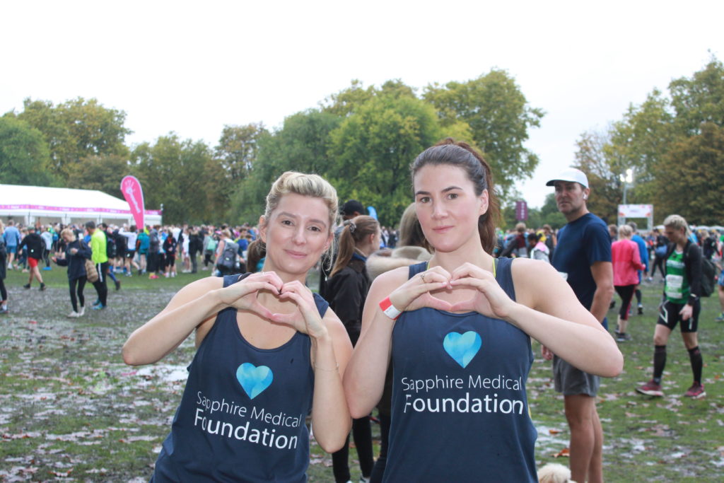 Two women wearing blue Sapphire Medical Foundation t-shirts pose for a photo at a fundraising event to provide financial assistance to medical cannabis patients. 