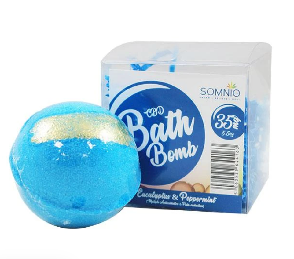 A blue bathbomb with a gold stripe on it in front of a box.
