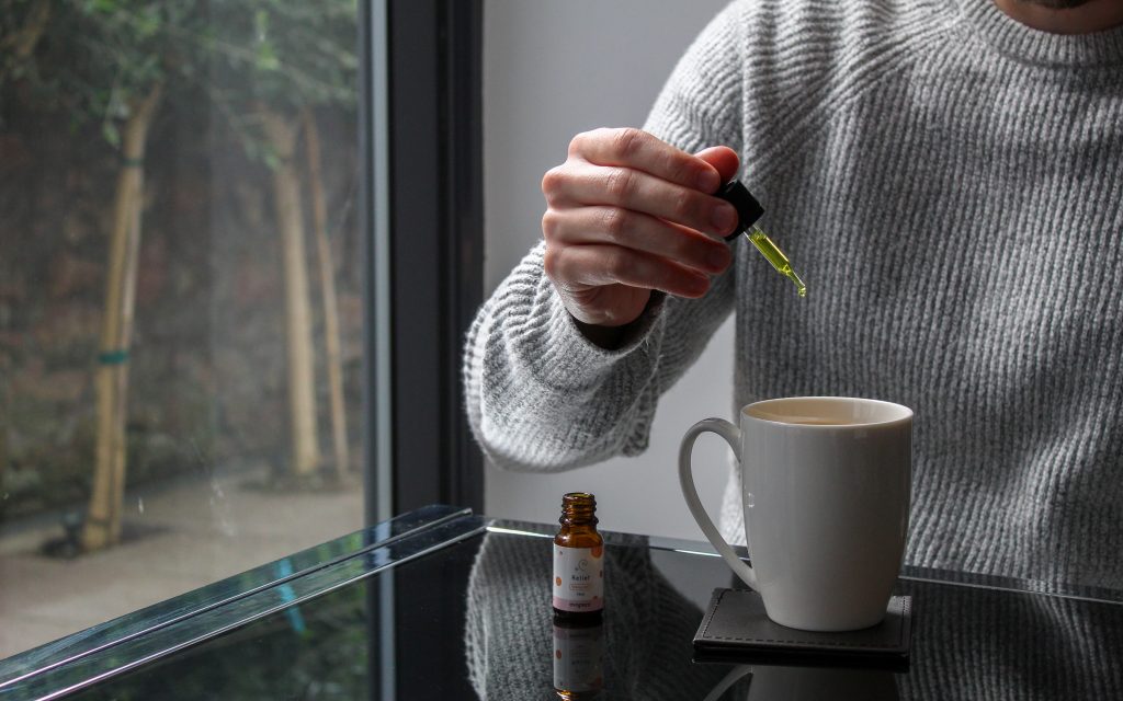 A person in a grey jumper drops a little bit of CBD into a cup of tea