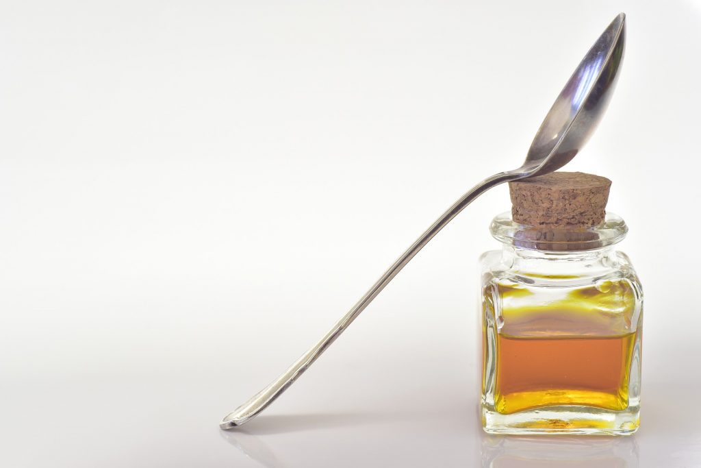 A small bottle of oil with a cork stopper in the top. A silver spoon leans against the bottle.