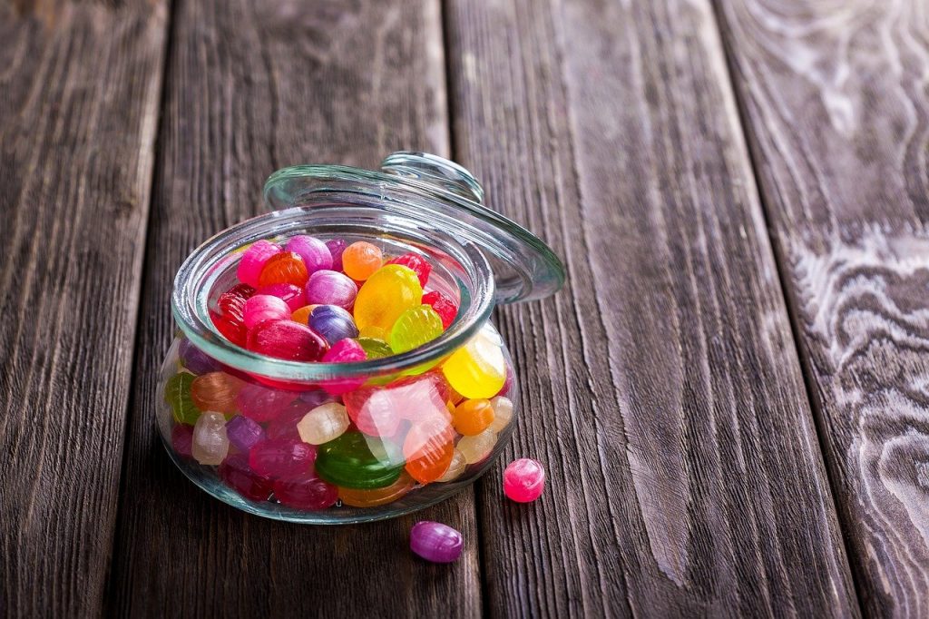 A small jar of brightly coloured sweets on a wooden surface