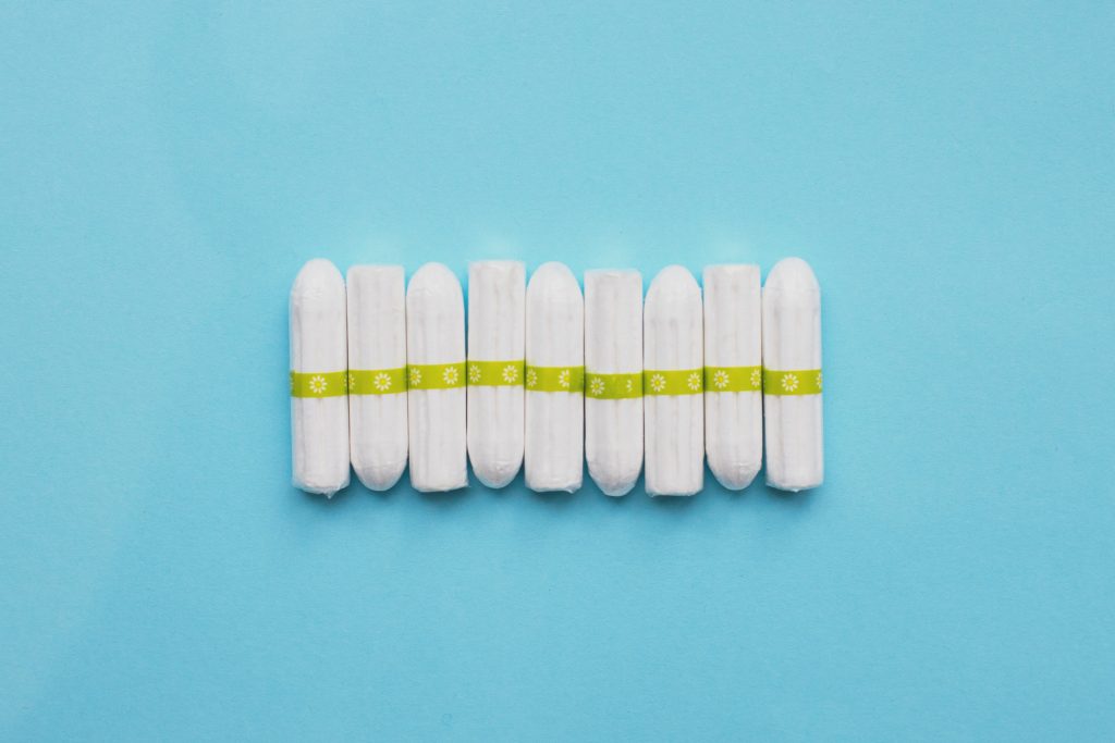 A row of white tampons on a blue background. The tampons have a green stripe on the centre