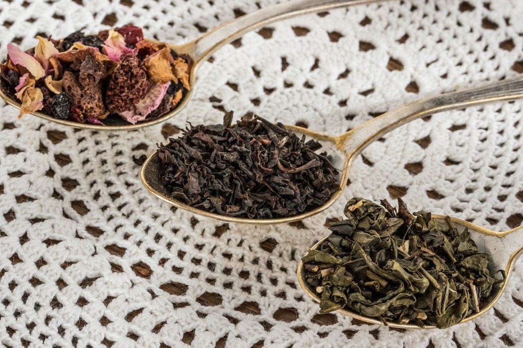 Three teaspoons in a row with different herbs on them resting on a lace placemat