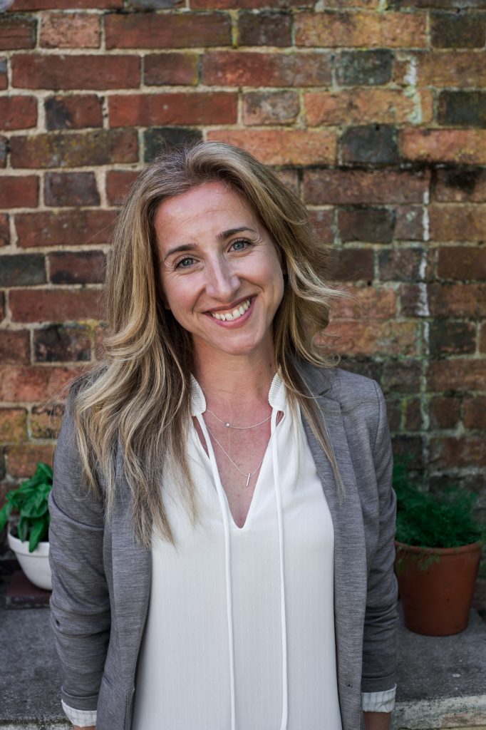 A women with globe hair wears a grey jacket as she smiles for a photograph 