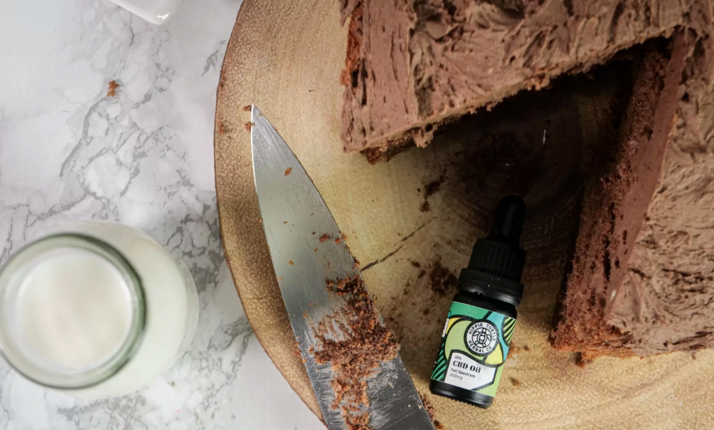 A chocolate cake on a wooden tray with a knife and some CBD oil