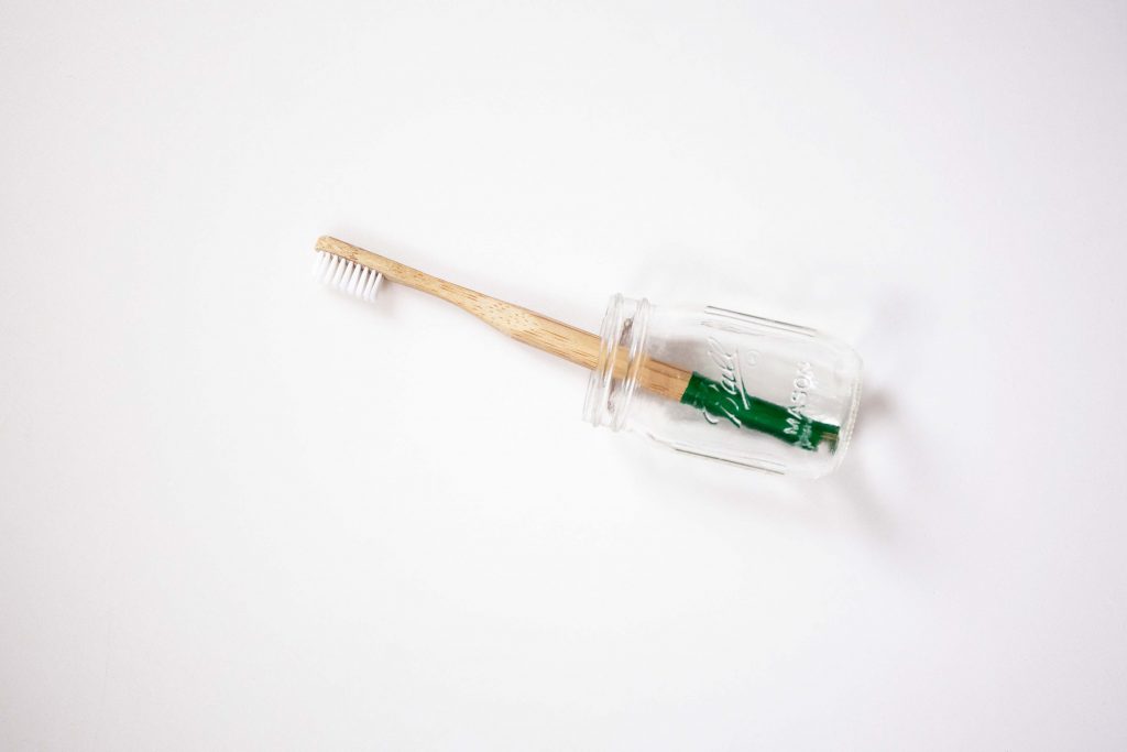 A wooden toothbrush lying on a white background in a glass jar. 
