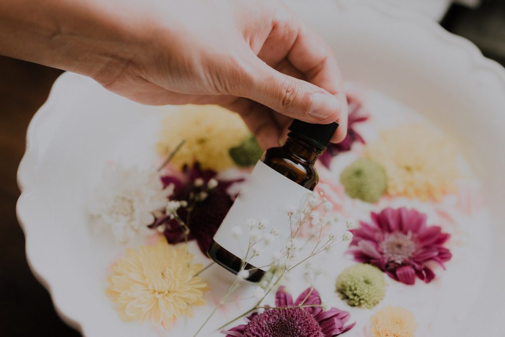 A hand holding a brown bottle of oil over a basin of flowers in white water