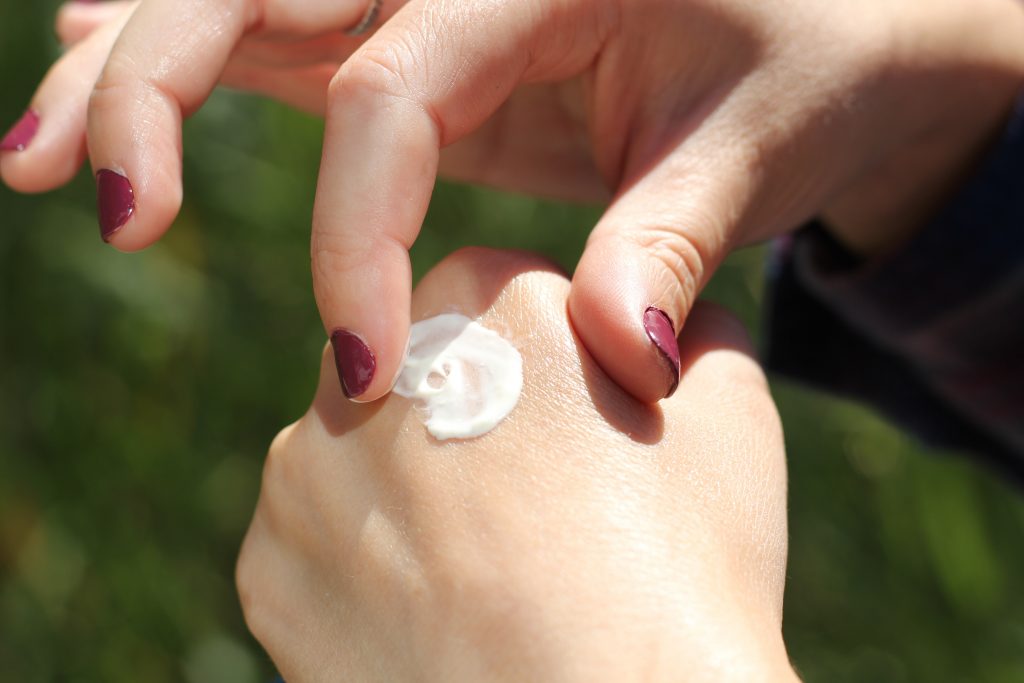 A hand with maroon red nails rubbing a white cream into the back of another hand