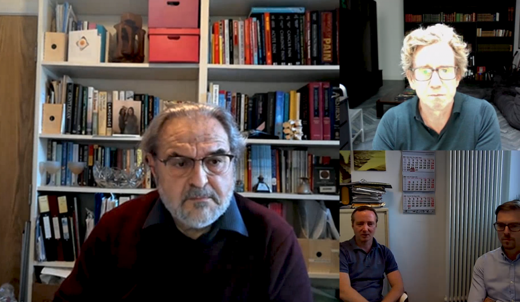 A zoom discussion between three different panels. One man sits infront of a bookcase. Another two men are in the lower half of the screen in front of a window while a third man sits above.